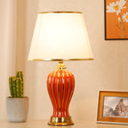 Red ceramic table lamp with gold trim, lit, with cactus and framed photo
