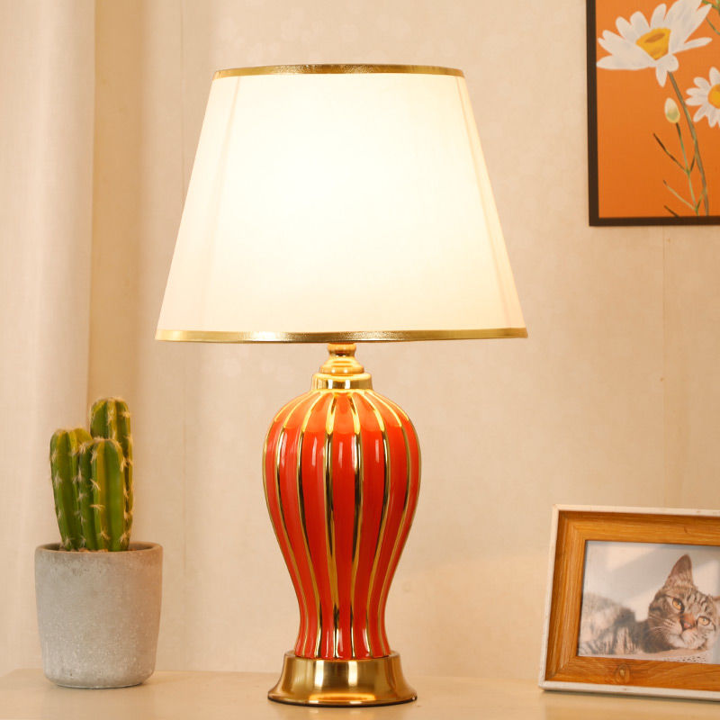 Red ceramic table lamp with gold trim, lit, with cactus and framed photo