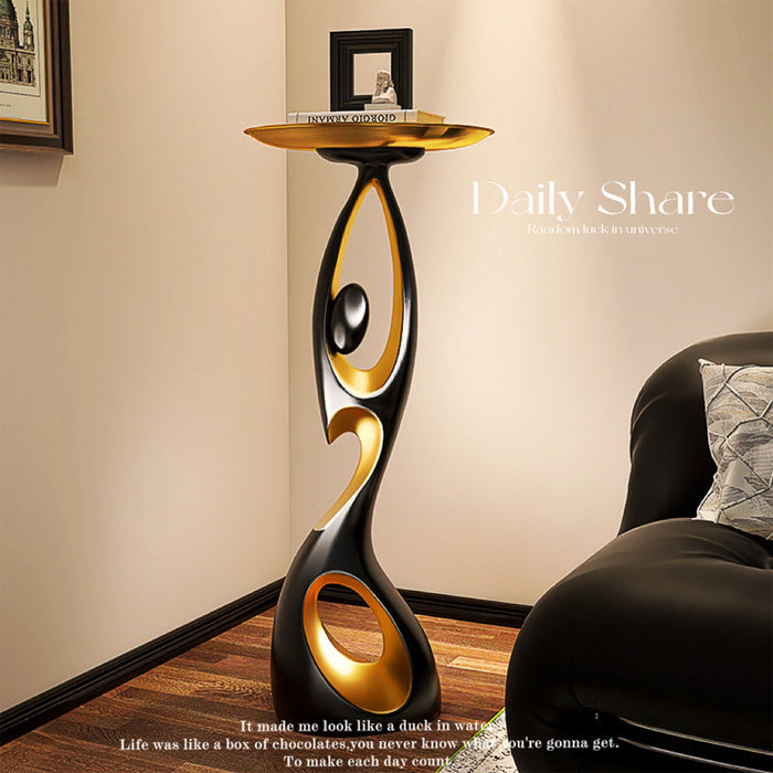 Black and gold Dancing Life resin floor ornament with round tray top beside a leather sofa