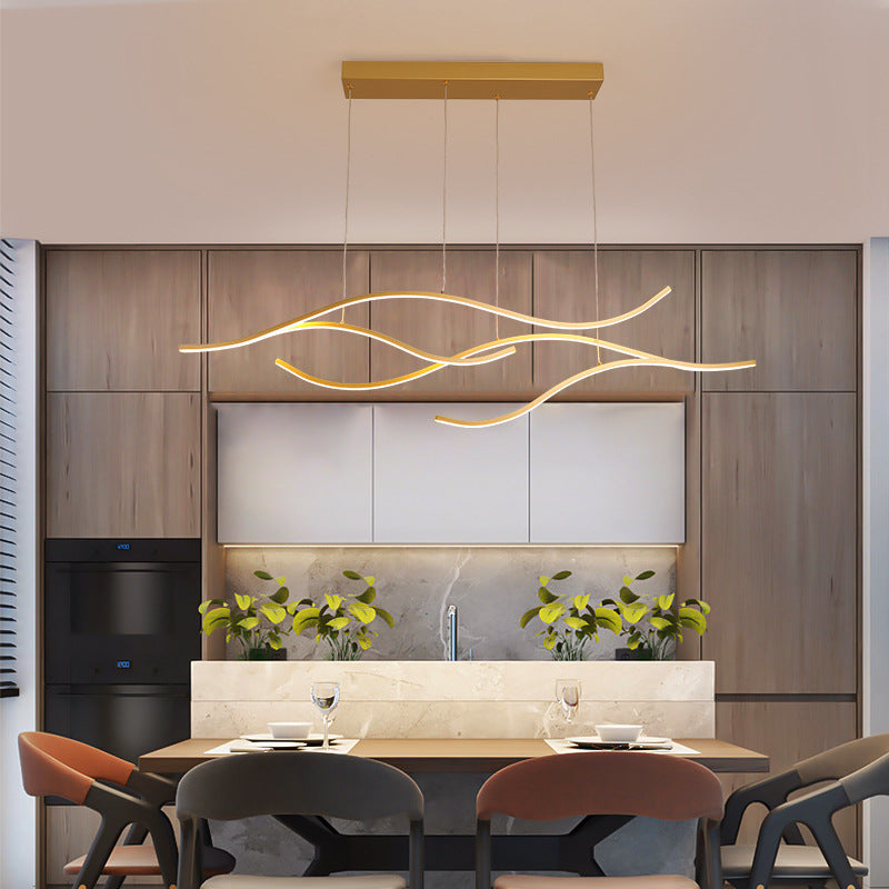 DRAPMODE modern gold LED pendant light with wavy linear design hanging over a contemporary dining table