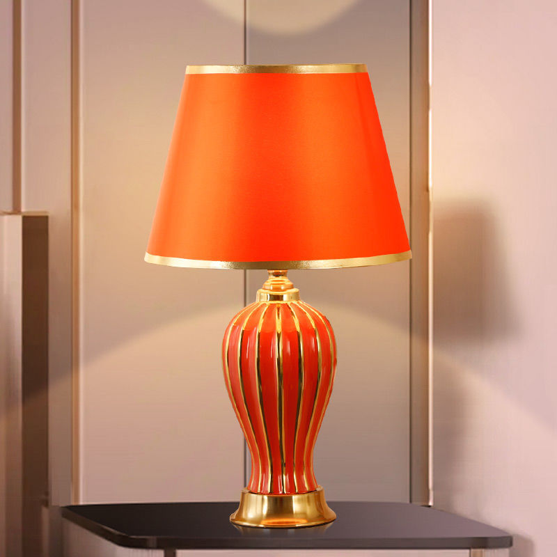 Red ceramic table lamp with gold-striped fluted base and red shade, lit on a dark side table