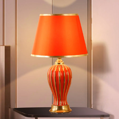 Red ceramic table lamp with gold-striped fluted base and red shade, lit on a dark side table