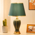 Green ceramic table lamp on a side table with a potted cactus and framed photo