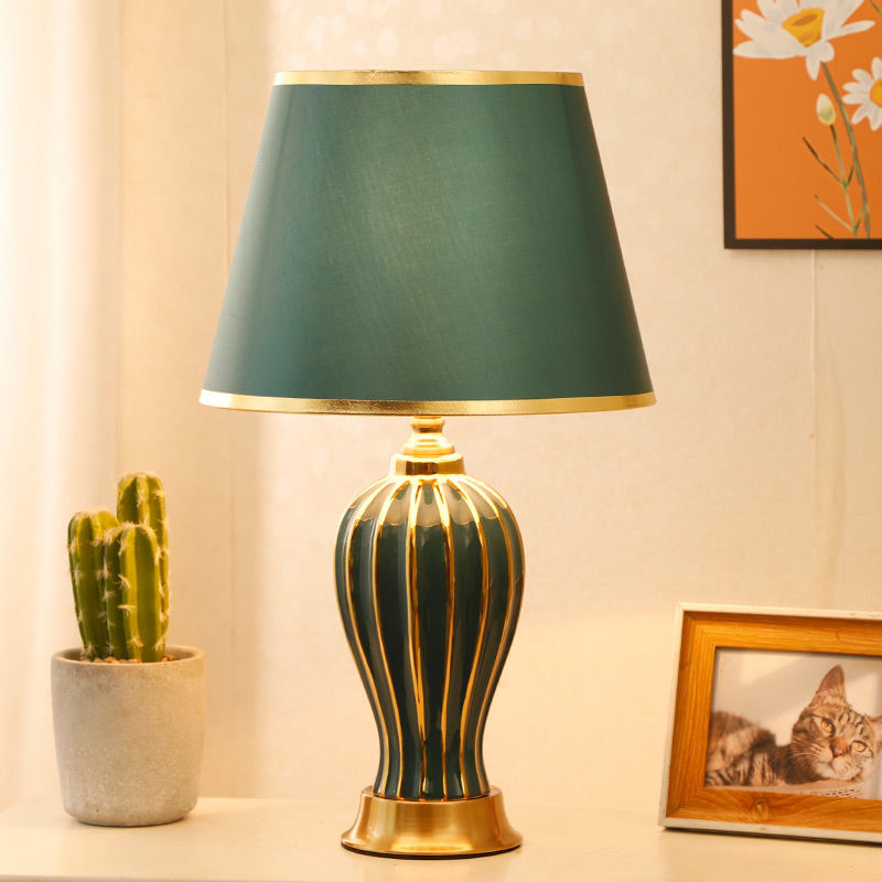 Green ceramic table lamp on a side table with a potted cactus and framed photo