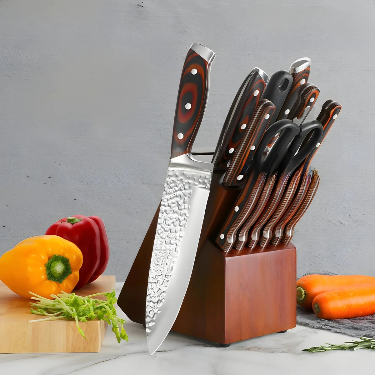 A kitchen knife set with a wooden block stand, featuring a large chef's knife with a hammered blade and several smaller knives with dark handles, styled with fresh vegetables on a marble surface against a gray background.
