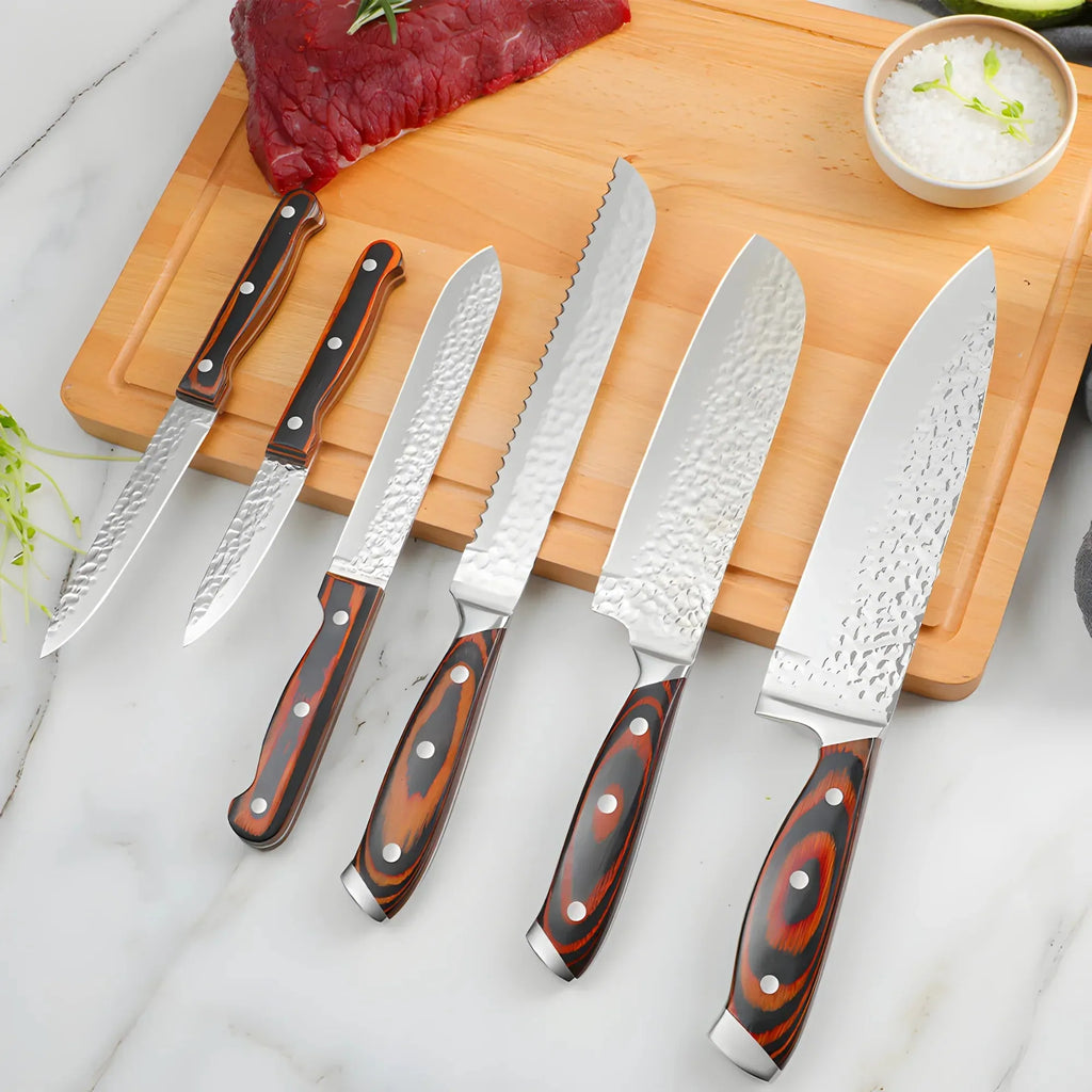 A 6-piece kitchen knife set with hammered and satin steel blades and reddish-brown wood handles, arranged on a wooden cutting board over a white marble surface with raw beef and a small bowl of salt.
