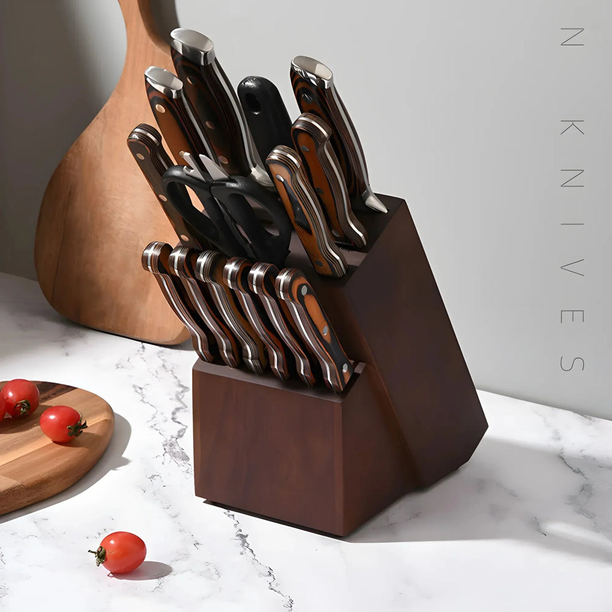 A dark wood knife block filled with kitchen knives, styled on a white marble countertop with tomatoes and a wooden cutting board nearby.