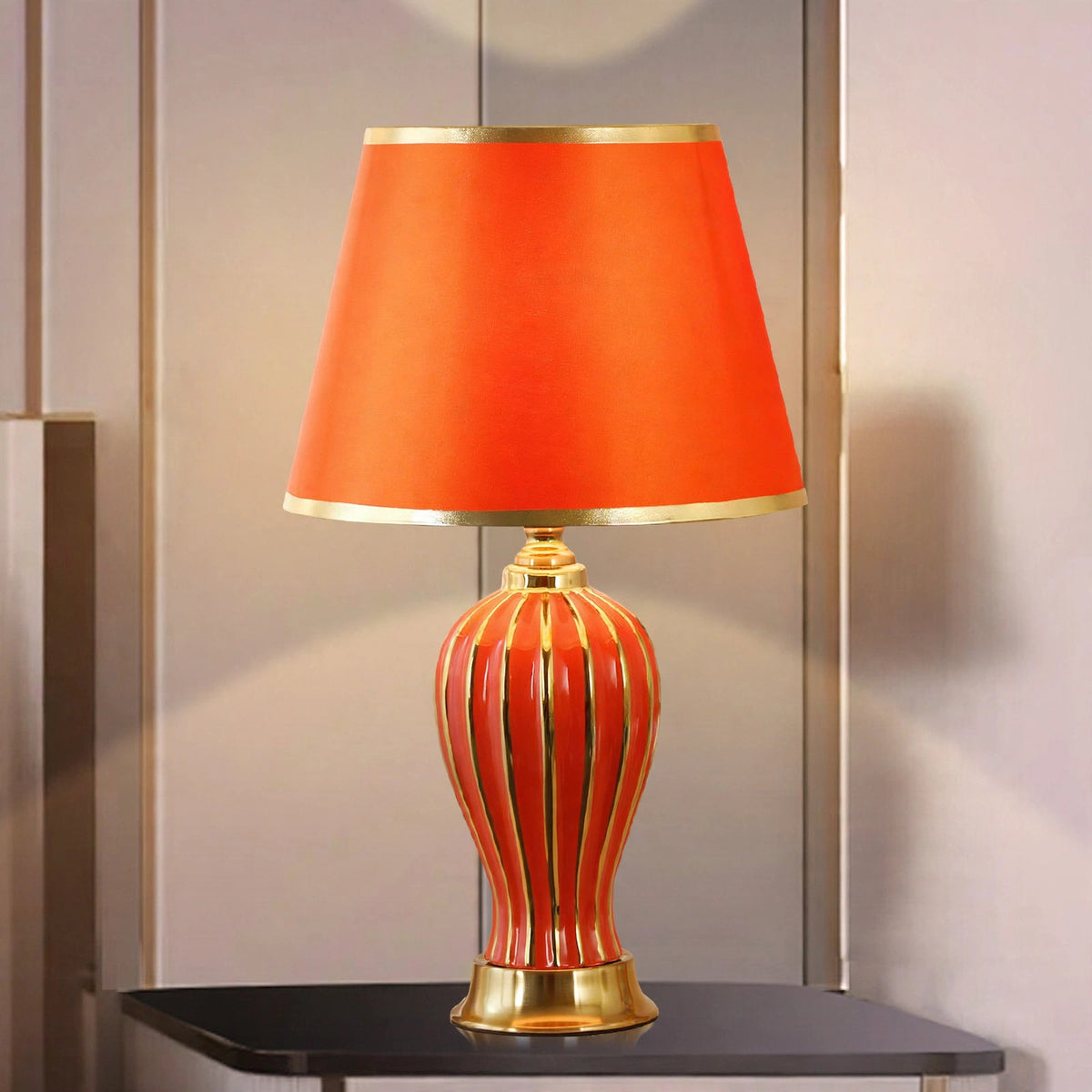 Red ceramic table lamp with gold-striped fluted base and red shade, lit on a dark side table