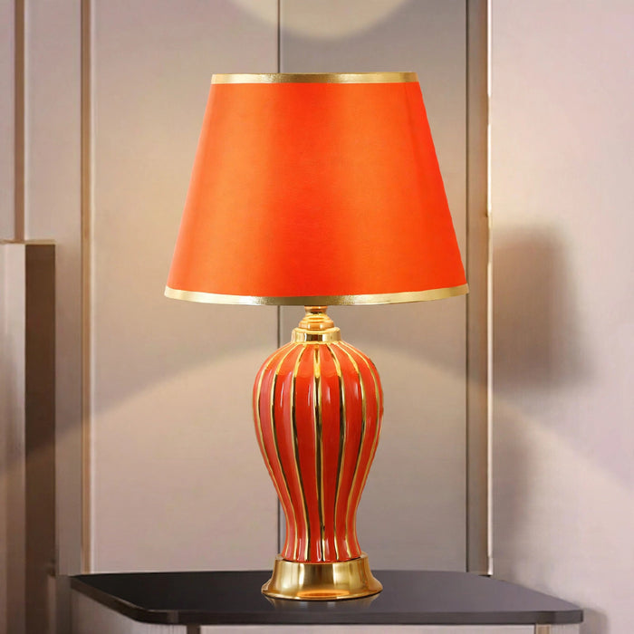 Red ceramic table lamp with gold-striped fluted base and red shade, lit on a dark side table