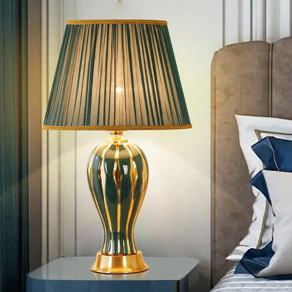 Green ceramic table lamp with pleated shade on a bedside table, lit