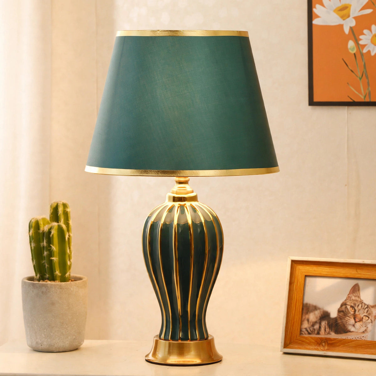Green ceramic table lamp on a side table with a potted cactus and framed photo